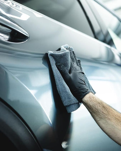 Person cleaning a car door with a microfiber cloth and black gloves