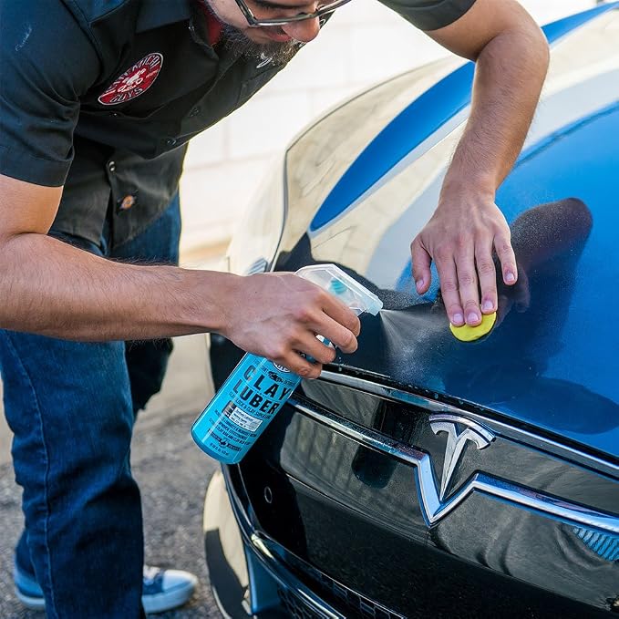 Person applying a product to a Tesla car with a spray bottle labeled 'City Lubricant'.